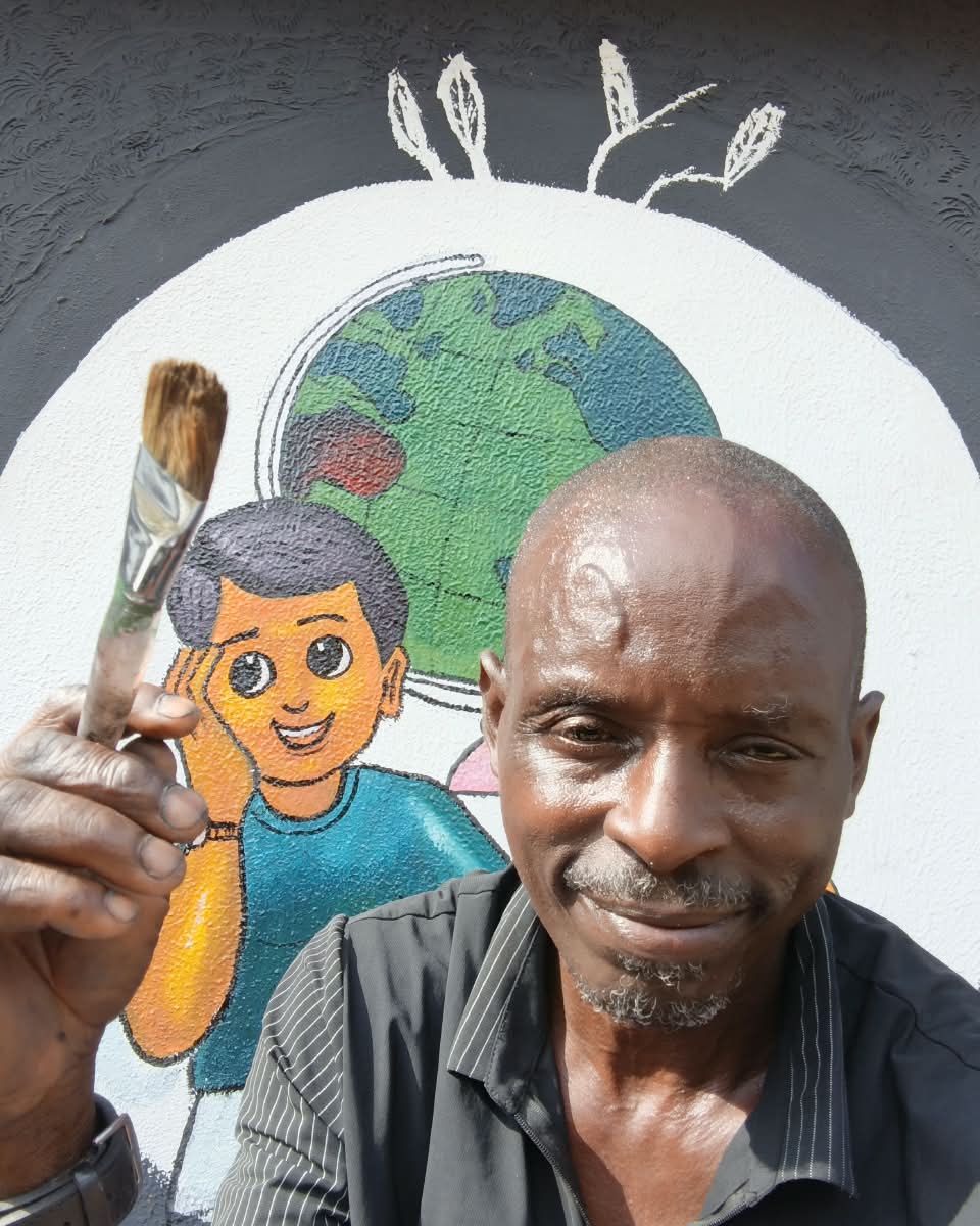 Odilli Gabriel holding a paintbrush in front of a school mural of a boy and a globe