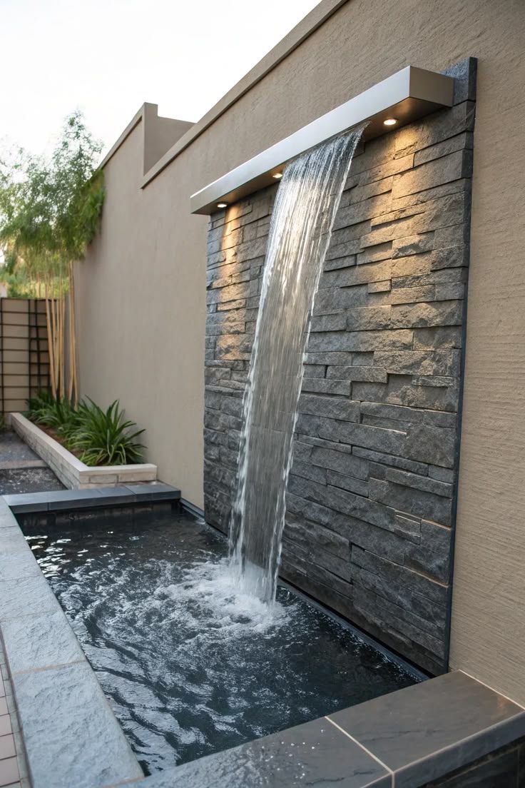 Outdoor waterfall pouring from a steel spout over a stacked-stone wall into a pool