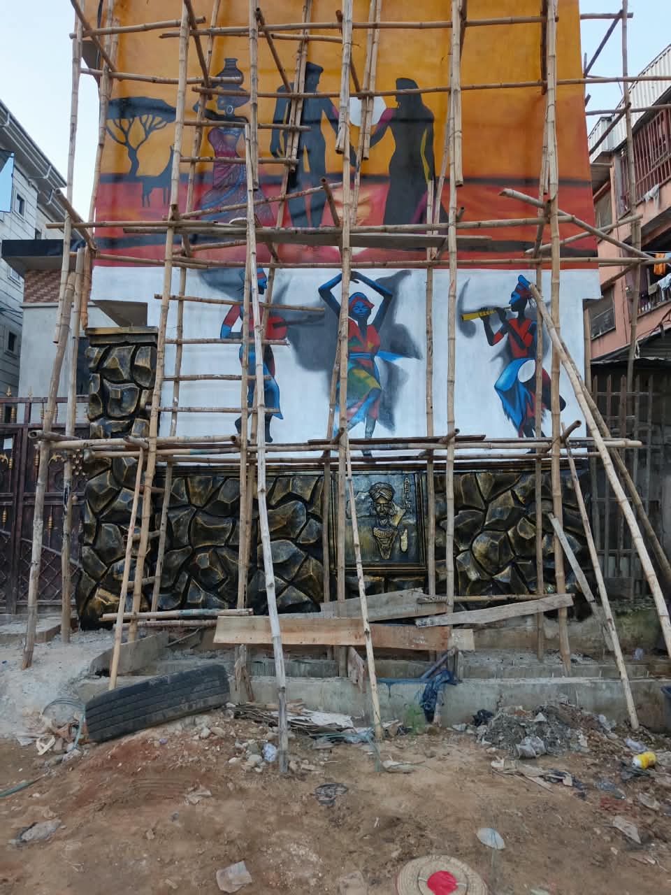 Exterior mural of dancers and musicians above a rock-textured relief wall