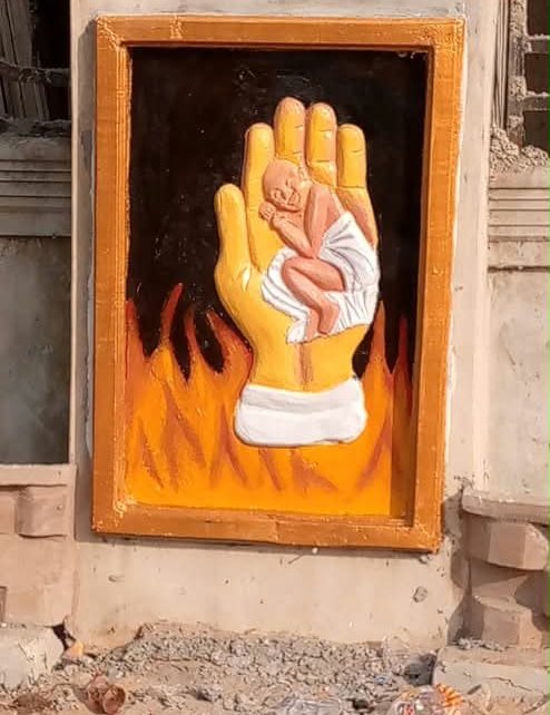 Framed painted relief of a hand holding a sleeping baby above flames