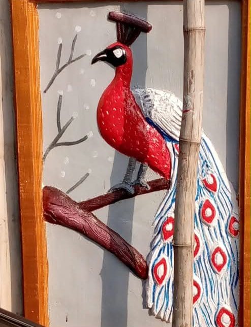 Framed relief of a red peacock on a branch with a long blue and white tail